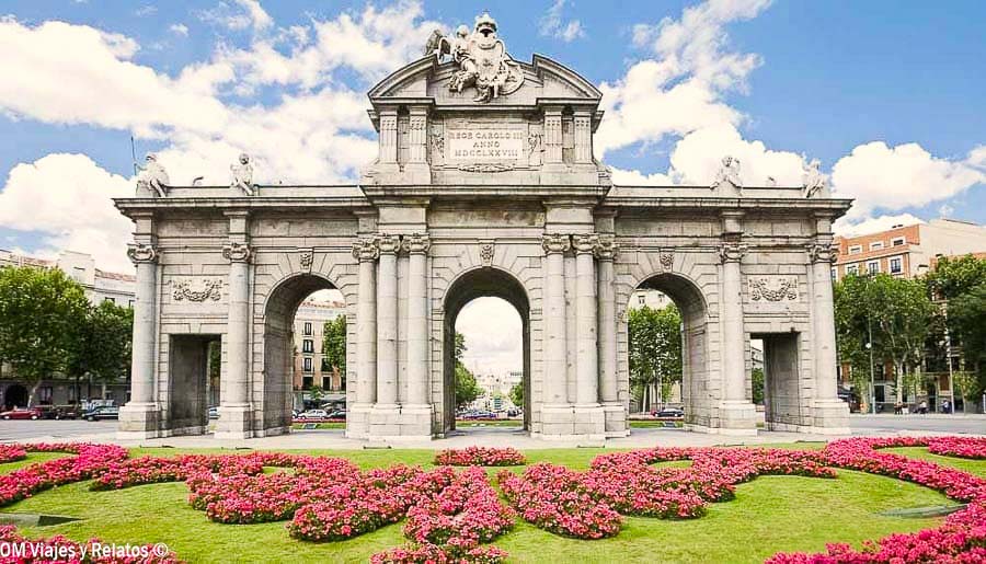 Puerta de Alcalá de Madrid con sus cinco arcos y jardines de flores rosas en primer plano