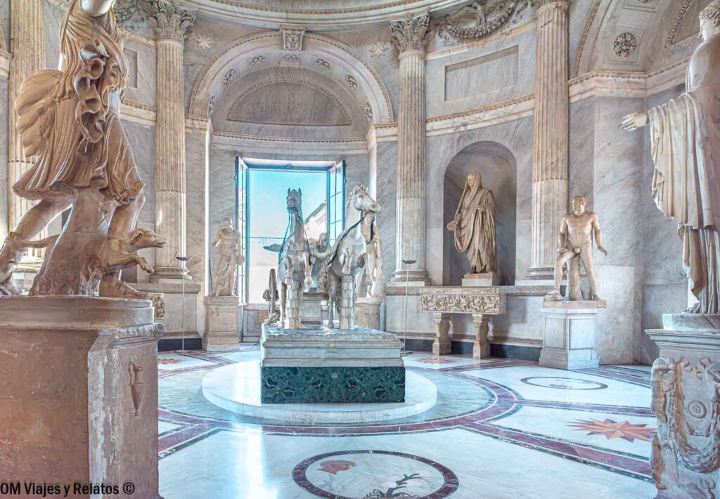 Sala de la Biga de los Museos Vaticanos, con un carro romano tirado por dos caballos y esculturas clásicas de mármol