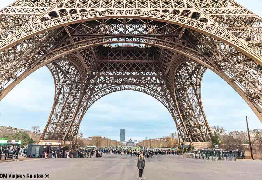 Vista de la Torre Eiffel desde abajo, con su impresionante estructura metálica y una viajera bajo sus grandes arcos
